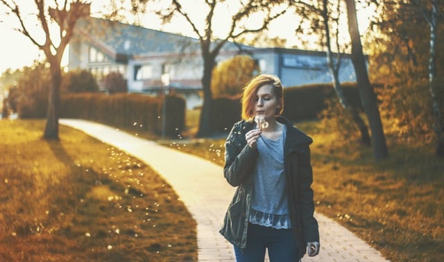 Mladá žena na ulici, je jeseň, v pozadí vidieť oranžové lístie na zemi. Žena fúka do bublifuku.